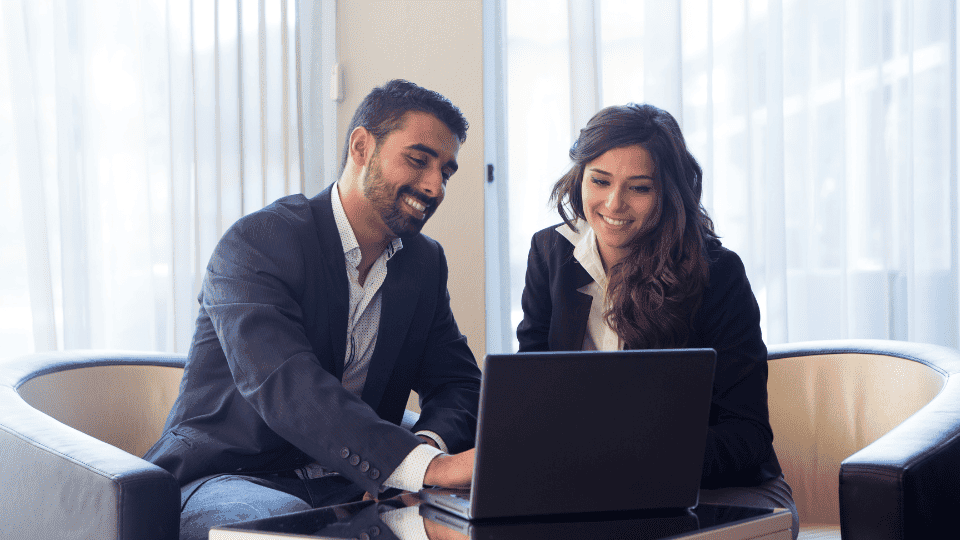 A man and woman smiling and looking at a laptop