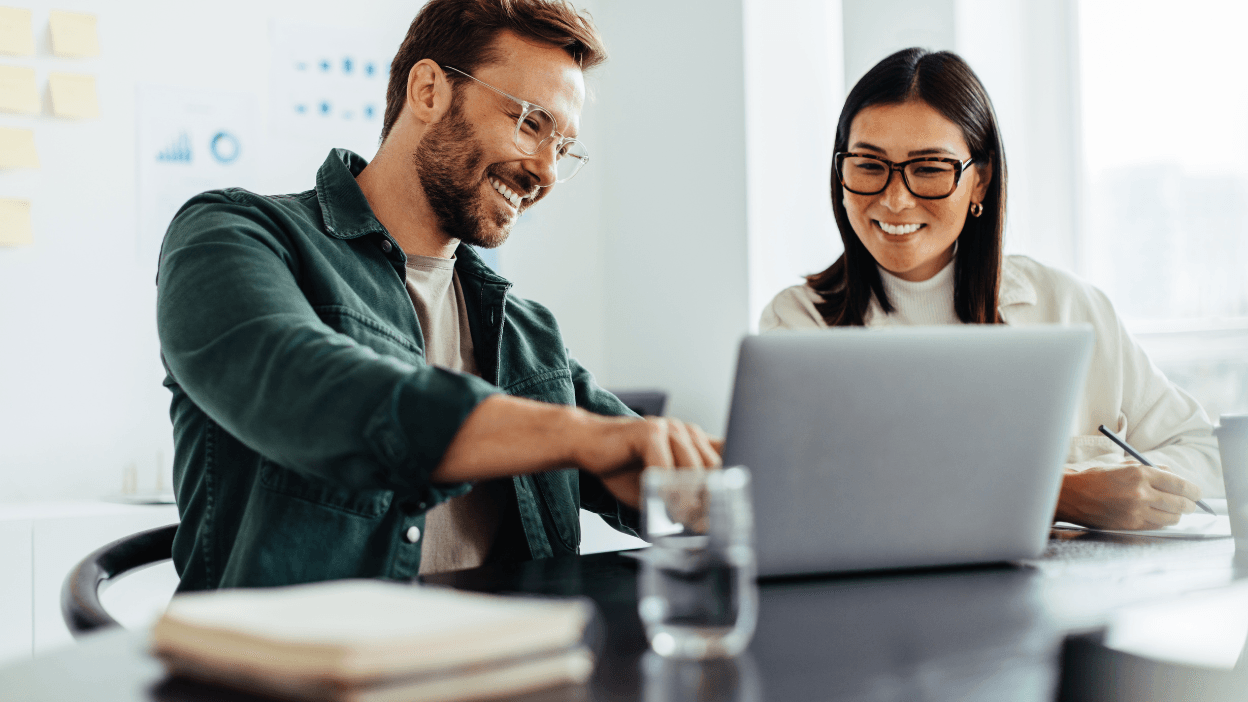 A man and woman smiling and looking at a laptop