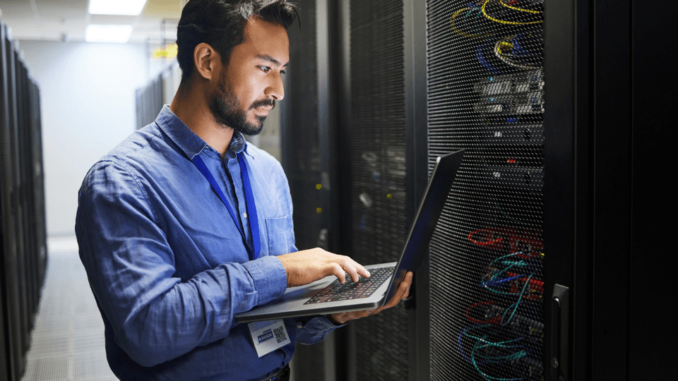 man checking laptop besides a mainframe