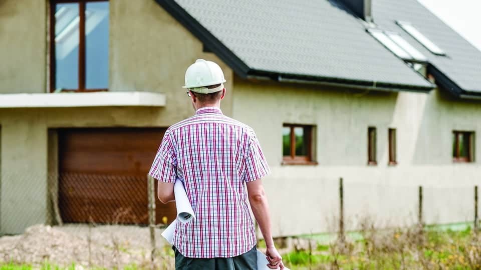 building contractor holding technical drawings in front of a housing development