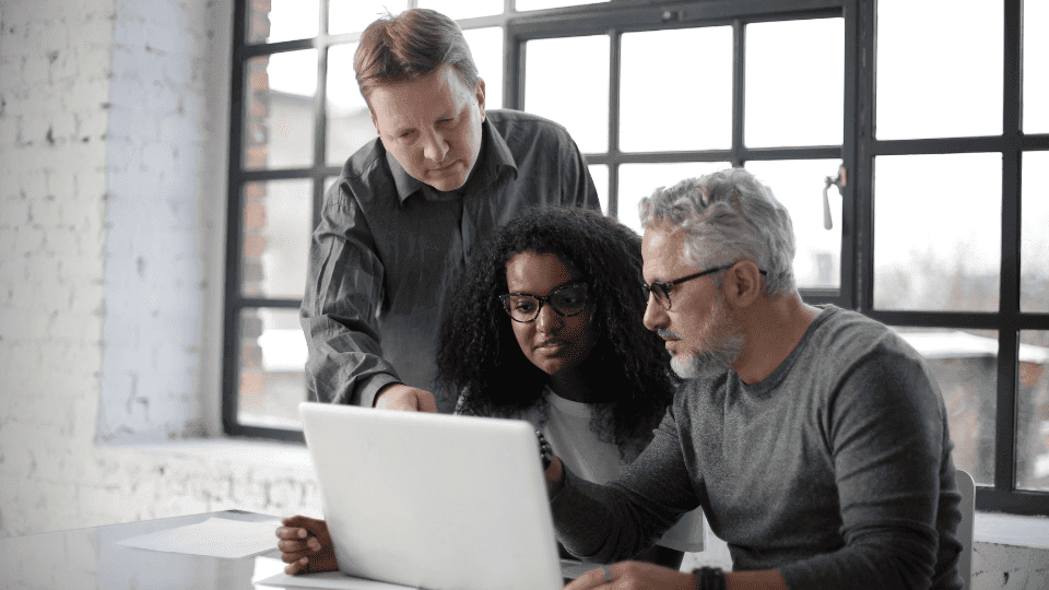 Two men and a woman looking at a laptop