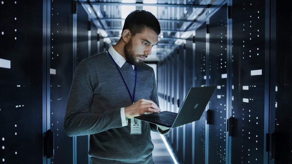 man in a server room looking at a laptop